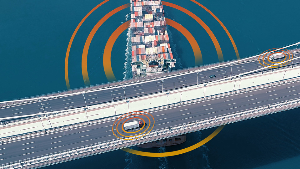Aerial view of a container ship passing beneath a bridge while trucks travel above it, with orange concentric circles highlighting the vehicles to represent monitoring, verification, and connected trust across the freight ecosystem.